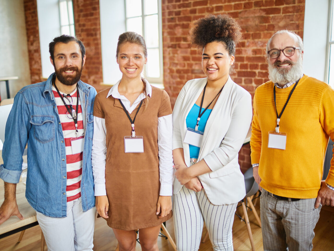 Four successful office managers with badges standing in front of camera and looking at you with smiles