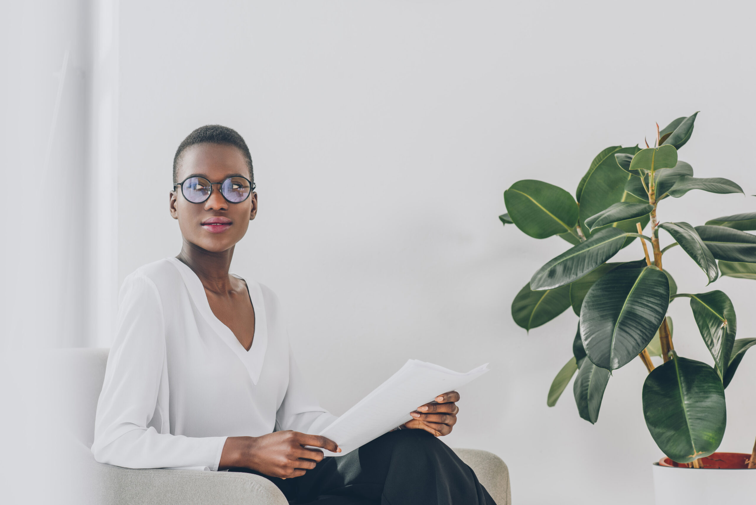 stylish attractive African American businesswoman sitting in armchair with documents in office