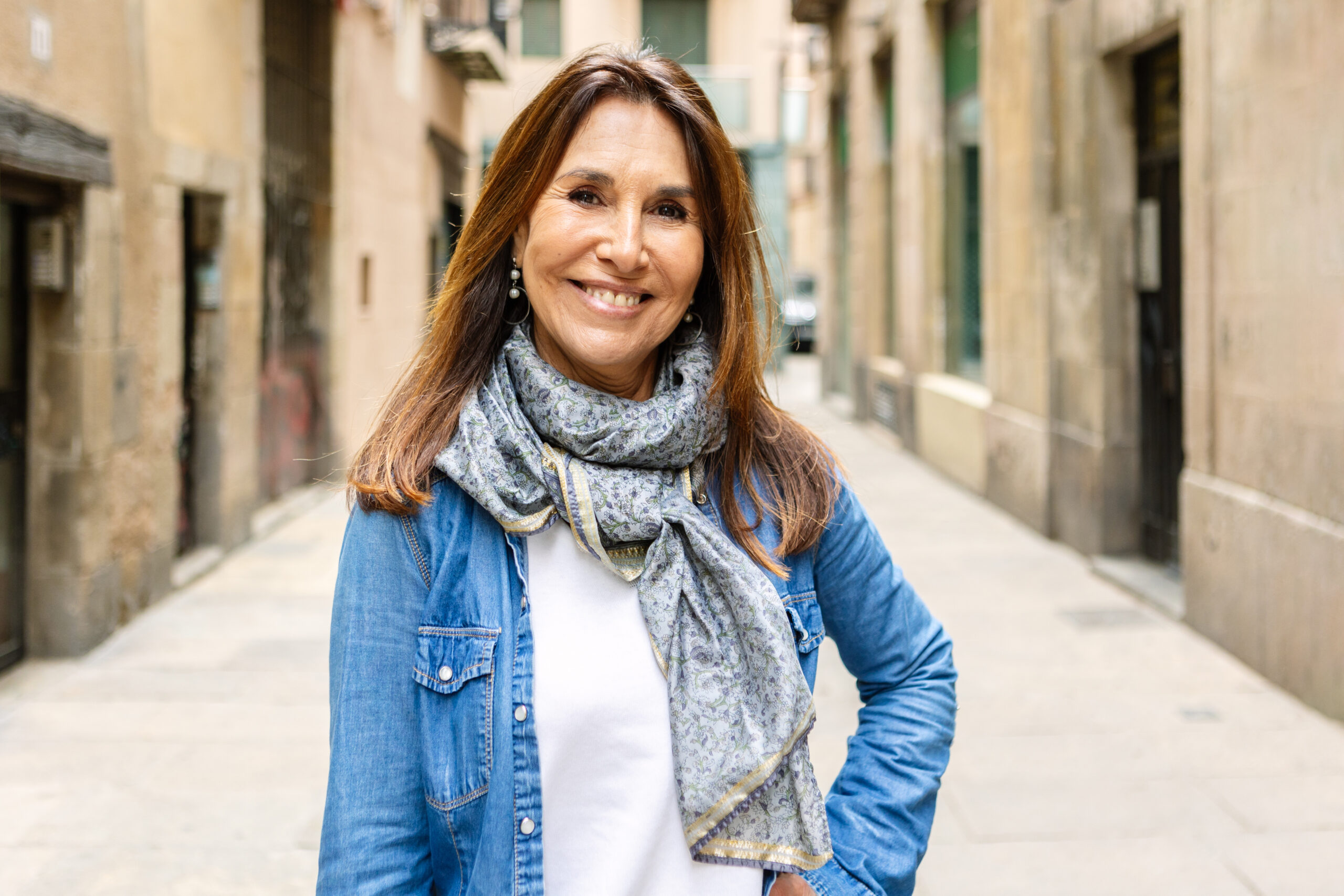 Smiling portrait of senior 50s middle aged woman looking at camera. Happy mature lady standing outdoors. Outside head shot at city street.