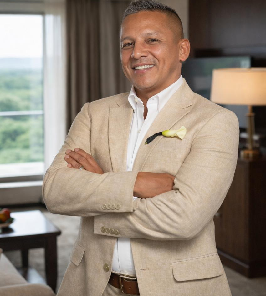 Alberto Gerardini, Senior Sales Leader, smiling in a beige suit with arms crossed in a professional office setting
