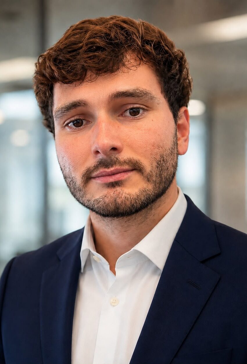 Professional headshot of Axel Rojas, licensed health insurance agent at Affordable Care Agents, wearing a navy blue suit and white dress shirt in a modern office setting.